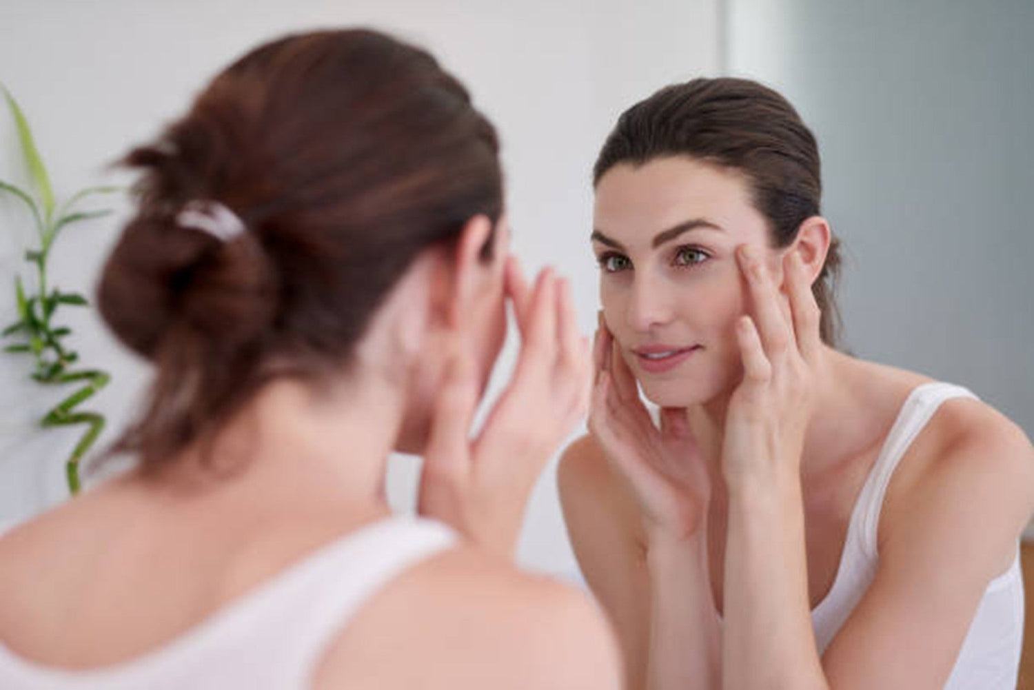 Woman touching her clean face while looking in the mirror.