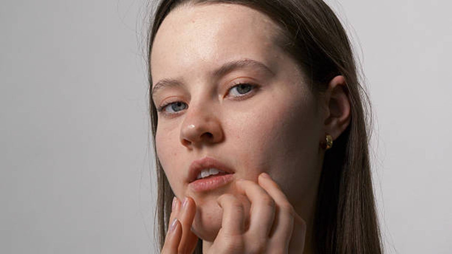 Woman gently touching her face while checking for dry and oily areas.